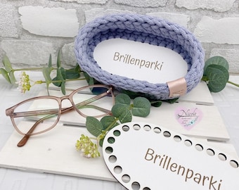 Op de afbeelding: Een lichtblauwe, gevlochten garenmand met de tekst "Brillenparki" op een witte inleg. Een bruin montuur bril en een houten basis met dezelfde tekst zijn ook aanwezig. De mand staat op een wit oppervlak.