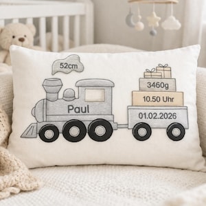 Puede incluir: Cojín decorativo crema con un diseño de tren gris y el nombre "Paul". El cojín incluye detalles bordados como la longitud del bebé (52cm), el peso (3460g), la hora (10.50 Uhr) y la fecha (01.02.2026).