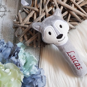 May include: Grey plush wolf rattle with the name "Lucas" embroidered in red on the handle.