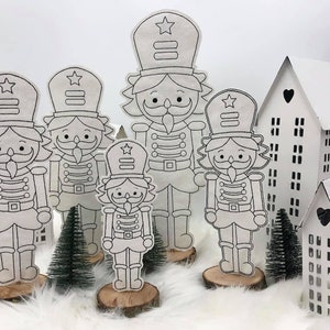 May include: Five black and white nutcracker figurines with a star on their hats. The figurines are standing on wooden bases. There are two white houses with black windows in the background.