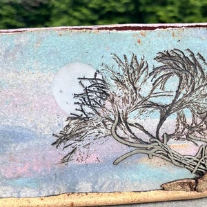 May include: Rectangular ceramic planter with a hand-painted landscape design. The artwork features a full moon, a stylized tree, and a pastel sky in shades of blue, pink, and white. The base and rim are a warm, earthy tone.