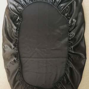 May include: Black satin fitted sheet with elastic all around the edges. The sheet is made of a soft, smooth fabric.