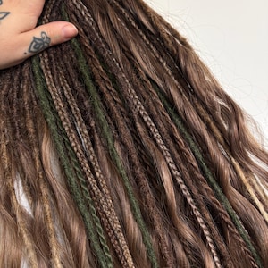 May include: A set of hair extensions featuring a mix of wavy brown strands, braided sections, and dark olive green yarn wraps. The hair pieces are arranged in a cascading style, showcasing varied textures including smooth waves, tight braids, and fuzzy yarn accents.