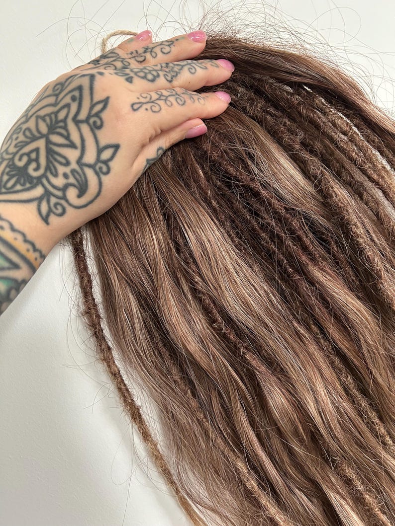 May include: Brown and light brown dreadlocks, with a natural, textured appearance. The dreadlocks are shown against a white background. The image shows the dreadlocks in a close-up view.