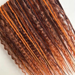 May include: A set of brown and orange synthetic dreadlocks. The dreadlocks are wavy and have a variety of textures.