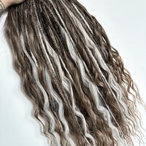 May include: Brown and white dreadlocks with wavy ends. The dreadlocks are a mix of brown and white strands, creating a natural, textured look. The hair is styled in a wavy pattern.