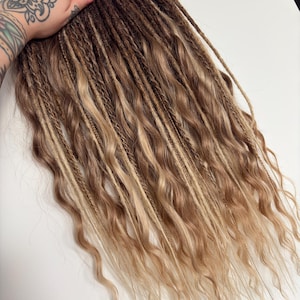 May include: A bundle of brown, blonde, and light brown dreadlocks with wavy ends. The dreadlocks are a mix of colors, creating a natural, highlighted effect. The hair is styled in a layered pattern.