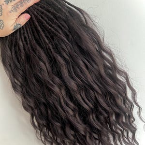May include: Dark brown synthetic dreadlocks with a wavy texture. The dreadlocks are long and thick, and they are arranged in a loose, flowing style.
