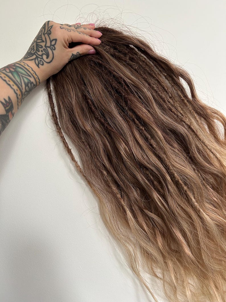 May include: A bundle of brown and blonde dreadlocks. The dreadlocks are a mix of dark brown and lighter blonde shades, with a natural, textured appearance. The hair extensions are styled in a wavy pattern.