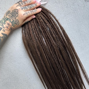 May include: A bundle of brown synthetic dreadlocks with a pink ribbon tied at the top.