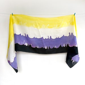 May include: A yellow, white, purple and black silk scarf with the text "Love is Love is Love is Love" printed on it.