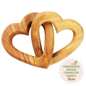 Könnte beinhalten: Zwei ineinander verschlungene, herzförmige Objekte aus hellbraunem Holz mit sichtbarer Maserung. Ein kleines kreisförmiges Etikett in der Ecke enthält den Text KASSIS, VERBUNDENE HERZEN, CONNECTED HEARTS und 5cm, was die Größe des Objekts angibt.