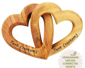 May include: Two interlocking wooden hearts carved from light brown wood with visible grain patterns. Each heart features the black engraved text "Text (custom)" on its surface. The hearts are connected in a continuous loop design.