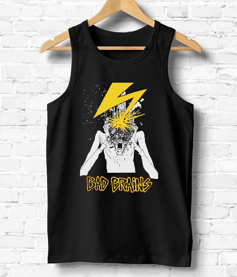 May include: Black tank top with a white graphic of a person with a city exploding out of their head. The graphic is surrounded by a yellow lightning bolt. The text "BAD BRAINS" is printed in yellow below the graphic.