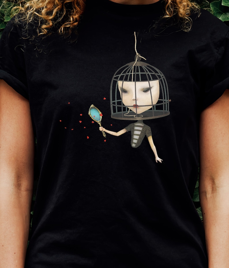 K&ouml;nnte beinhalten: Schwarzes T-Shirt mit einem grafischen Druck einer Frau mit einem Vogelk&auml;fig auf dem Kopf. Sie h&auml;lt einen Spiegel und rote Herzen schweben um sie herum.
