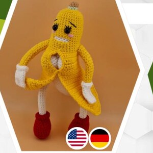 May include: A handmade crochet banana character with a yellow peel, white gloves, red shoes, and a smiling face. The banana has a brown top and is standing on a beige surface. The character is a whimsical, playful design.