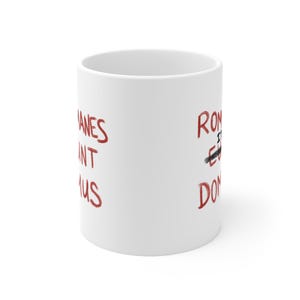 May include: White ceramic mug with red text that reads "Romans" with the "o" crossed out and "Romans" written below. On the other side of the mug, the text reads "Romans" with the "o" crossed out and "Don't" written below.