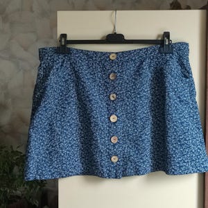 May include: A blue skirt with a white floral pattern and a row of brown buttons down the front.