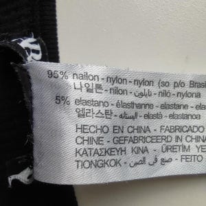 Puede incluir: Primer plano de una etiqueta de tela blanca con texto negro. La etiqueta indica una composici&oacute;n de material de 95% nailon y 5% elastano. Informaci&oacute;n adicional de fabricaci&oacute;n en varios idiomas, incluyendo espa&ntilde;ol y chino.