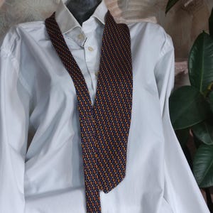 May include: A dark blue patterned tie with orange and white accents. The tie is made of silk and has a classic design.