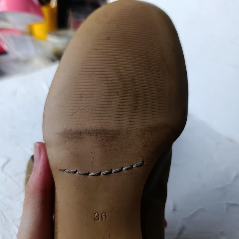 May include: Close-up of the sole of a shoe. The sole is a light brown color with horizontal grooves for traction. The number "36" is visible, indicating the shoe size. A stitched seam is present near the heel.