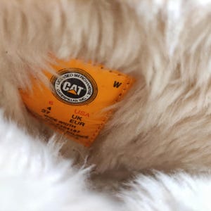 Może przedstawiać: Ż&oacute;łto-czarna etykieta z tekstem "LICENSED MERCHANDISE CAT CATERPILLAR INC." i literą "W" w białym k&oacute;łku. Etykieta zawiera r&oacute;wnież liczby "6", "4", "37", "USA", "UK", "EUR", "WIDE WIDTH", "P304107" i "BALANCE".