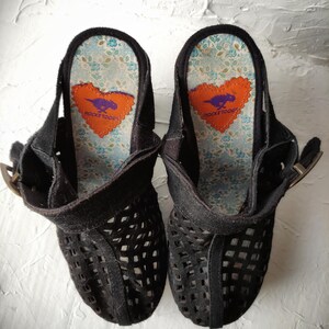 May include: A pair of black suede platform sandals with a cut-out design. The sandals have a heart-shaped logo on the insole that says "Rocket Dog".