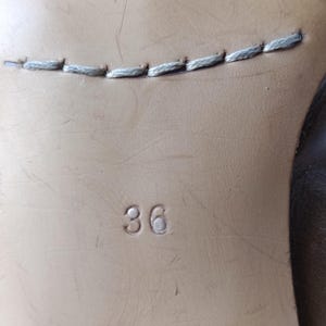 May include: Close-up of a shoe sole with the number "36" embossed on the light brown leather. A line of light gray stitching is visible near the top of the image. The shoe sole is likely from a pair of women's shoes.