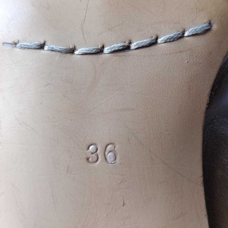 May include: Close-up of a shoe sole with the number "36" embossed on the light brown leather. A line of light gray stitching is visible near the top of the image. The shoe sole is likely from a pair of women's shoes.