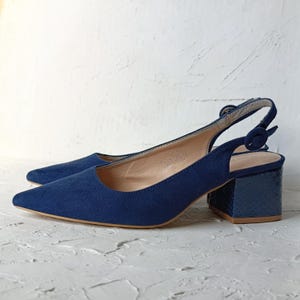 May include: A pair of navy blue slingback heels. The shoes have a pointed toe and a block heel with a textured, faux snakeskin pattern. The heel height appears to be approximately 3 inches.