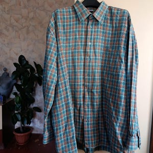 May include: A long-sleeved shirt with a teal, orange, and brown plaid pattern. It features a classic collar, a chest pocket, and buttoned cuffs. The shirt is made of a medium-weight woven fabric, suitable for various occasions.