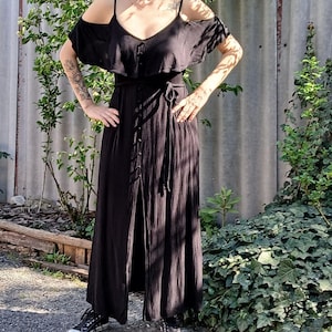 May include: A black maxi dress with a ruffled neckline and a tie belt. The dress has a front slit and is made of a lightweight fabric.