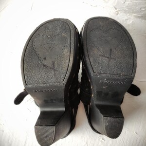 May include: A pair of black platform sandals with a heart-shaped design on the soles. The sandals have a buckle closure and are made by the brand "Rock & Roll Cowgirl".