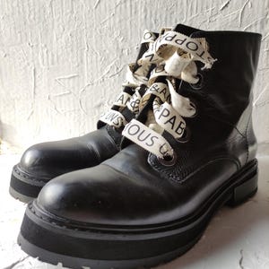 May include: Black leather ankle boots with a thick platform sole. The boots have white ribbon laces with the words "Topshop" and "Fabulous" printed on them.