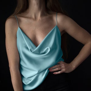 May include: A light blue satin top with a cowl neck and thin straps. The top is draped over the chest and falls loosely to the waist.