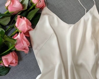 May include: A white silky tank top with thin straps. The tank top is laying on a black and white patterned surface with pink roses.