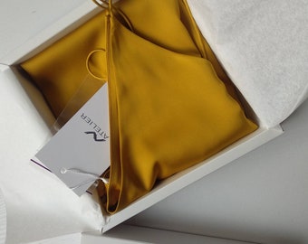 May include: A mustard yellow silk slip dress in a white box with a white tag that says "Atelier" in black lettering.