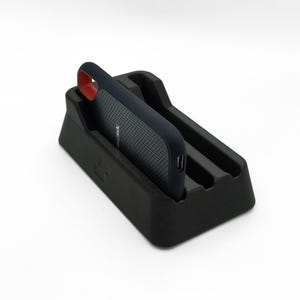 Könnte beinhalten: Schwarzer Telefonständer mit einem marineblauen Telefon in einer Hülle mit rotem Akzent. Das Telefon hat ein perforiertes Design und der Markenname "SanDisk" ist sichtbar. Der Ständer hat ein minimalistisches Design.