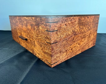 May include: A wooden box with a dark brown lid and a light brown body. The box has a small drawer with a wooden handle. The box is made of wood with a unique grain pattern.
