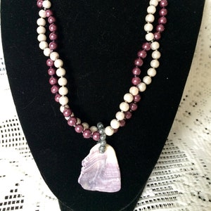 Può includere: Una collana a doppio filo con perline color borgogna e crema e un ciondolo a forma di conchiglia viola.