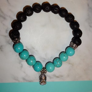 Puede incluir: Un brazalete de cuentas de lava negra y turquesa con un dije de Buda de plata.