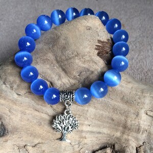 Pode incluir: Um bracelete de pedras azuis com um fecho de árvore de prata. O bracelete é feito de contas redondas e tem um fecho de prata.