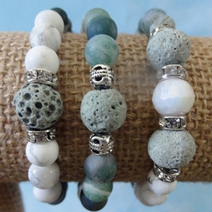 May include: Three bracelets with different beads. The first bracelet has white and grey beads. The second bracelet has green and grey beads. The third bracelet has white, grey, and clear beads.