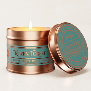 May include: A copper-colored candle tin with a teal label that reads "Frozen Forest." The lid is off, revealing the candle and a lit wick. The candle's scent is described as "Pomme Givrée, Pin et Mousse."