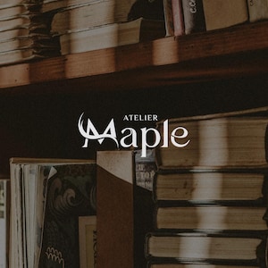 May include: A wooden bookshelf filled with stacks of old books, featuring a white logo in the centre that reads Atelier Maple. The books have worn, neutral-toned covers and are arranged in vertical and horizontal piles on dark wooden shelves.