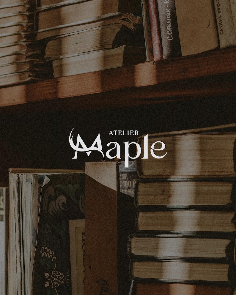 May include: A wooden bookshelf filled with stacks of old books, featuring a white logo in the centre that reads Atelier Maple. The books have worn, neutral-toned covers and are arranged in vertical and horizontal piles on dark wooden shelves.