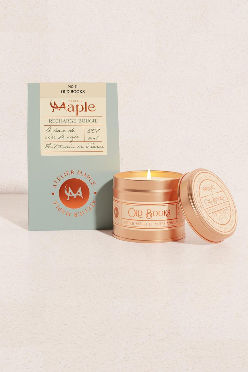 May include: A lit candle in a metallic copper tin labelled Old Books, accompanied by a rectangular sage green box. The box features the text Atelier Maple, No. 41 Old Books, and indicates a 250 ml volume. The candle lid rests beside the tin.