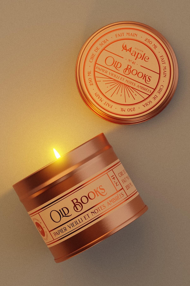 May include: A copper-coloured metal candle tin with a lit wick and a matching lid. The label reads "Atelier Maple", "Old Books", "N&deg;41", "Papier vieilli et notes ambr&eacute;es", "Cire de soja", "Fait main", and "250 ml". The candle emits a warm glow.
