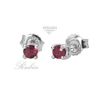 Puede incluir: Un par de pendientes de plata con una sola piedra de rubí roja en cada pendiente. Los pendientes están engastados en un diseño simple y elegante.