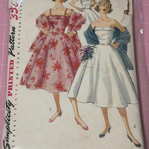 May include: Vintage Simplicity printed sewing pattern, size 14, bust 32. The pattern features illustrations of two dresses: a red floral print dress and a white strapless dress. The pattern is in a plastic sleeve.